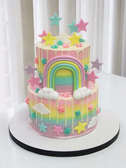 A two-tiered rainbow drip cake for a 2nd birthday. The pastel rainbow airbrushing, fluffy clouds, and colorful stars make this a truly joyful and dreamy celebration cake.