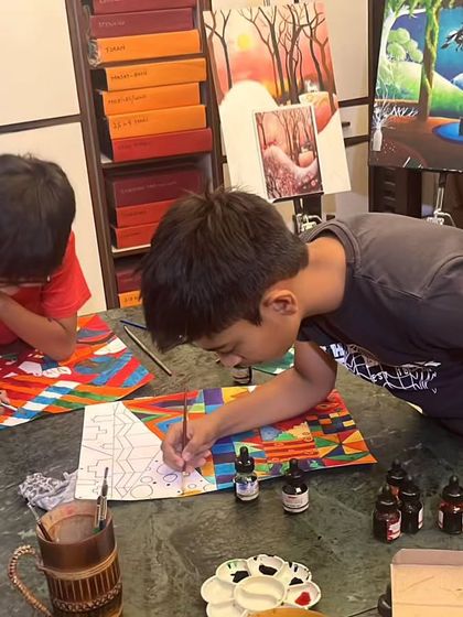 Two students busy at work creating intricate patterns for their African Kente cloth project. They are using ink and watercolors to achieve these beautiful, vibrant designs.