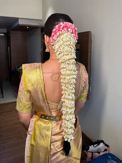 A traditional South Indian bridal hairstyle featuring a long braid fully covered in fresh jasmine flowers (gajra), with a touch of pink flowers at the top. This is a classic and fragrant choice for a wedding.