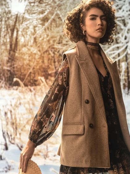 A snowy forest scene provides a cool, serene backdrop. The lighting is soft and diffused, complementing the wintery mood and the model's warm clothing.