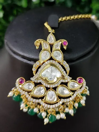 This stunning maang tikka features a unique shape with large kundan stones and delicate green and red accents.