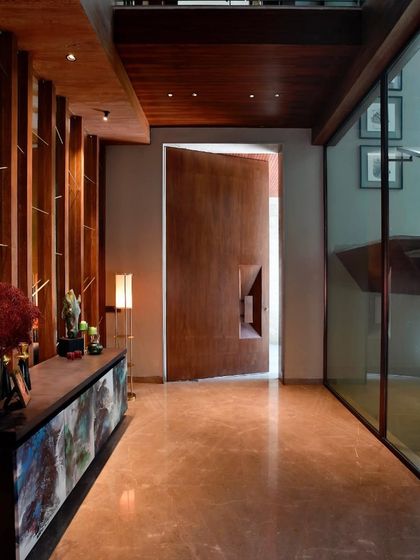The entrance of the T House in Gurgaon features a massive pivot door and a custom art-like credenza. The polished marble floor and warm wood tones create an entryway that is both grand and welcoming.