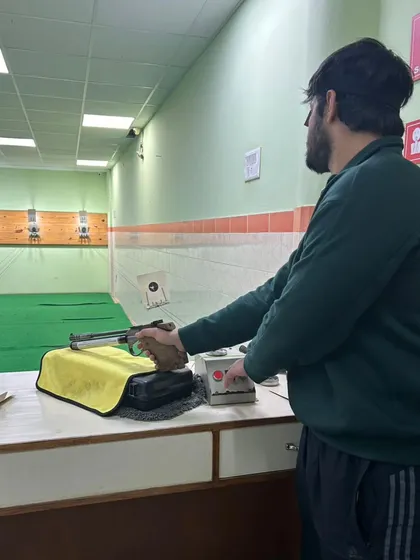A student preparing for his shot at the 10m air pistol range, carefully setting up his equipment.