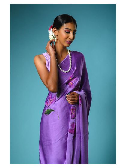 A three-quarter shot of the purple saree, focusing on the hand-painted details and the elegant pearl necklace. This image highlights both the garment and complementary accessories.