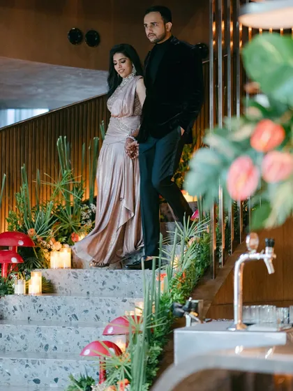 A couple makes a grand entrance down a staircase adorned with tropical florals and quirky mushroom props for their 'Citrus Safari' themed reception. We love creating immersive experiences that transport your guests.