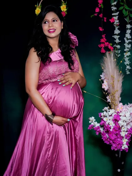 A classic three-quarter portrait of a mom-to-be cradling her bump. The simple floral background and elegant pink dress keep the focus entirely on her happy expression.