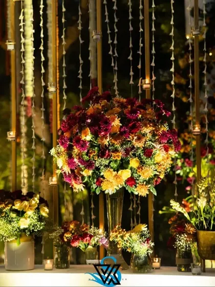 A stunning floral installation featuring a large bouquet of chrysanthemums and roses, set against a backdrop of hanging jasmine garlands and candles. This creates a rich, multi-layered visual and sensory experience.