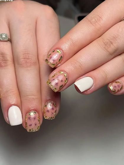 A creative design featuring a mix of solid white nails and translucent nails with dried flowers and gold foil encapsulated within.
