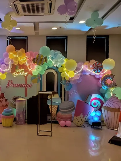 A wide shot of a Candyland party setup, showing the main backdrop and surrounding props like giant cupcakes and ice creams.