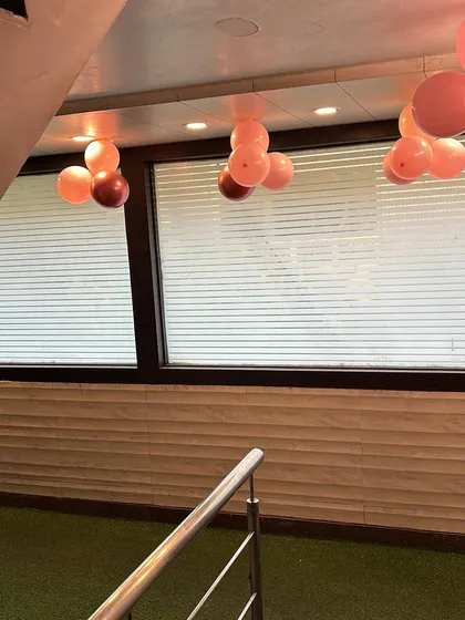 Part of an anniversary decor setup, showing simple balloon bunches hanging from the ceiling. These small details help fill the space and tie the whole look together.