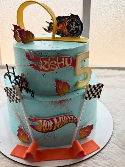 A two-tier Hot Wheels cake ready to race. This design features the iconic logo, checkered flags, and a track loop, making it the perfect birthday cake for a young car enthusiast.