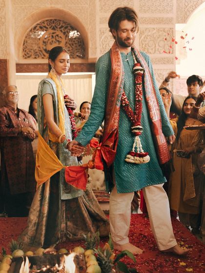 The couple takes their first steps as husband and wife around the sacred fire. This photo captures the motion and significance of the ritual, with guests looking on and showering them with petals.