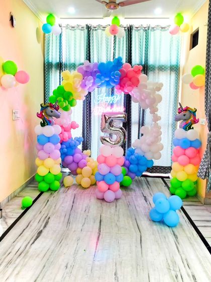 A full view of the unicorn-themed birthday decoration at home. The setup includes a circular balloon arch in pastel rainbow colors, a neon sign, and a number "5" foil balloon, transforming the living room into a fantasy land.