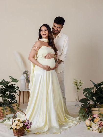 In our indoor garden setup, this couple shares a happy moment. The flowing dress and surrounding flowers add a soft, romantic feel to this studio maternity portrait.