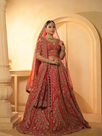 A majestic full-length portrait. The bride stands tall and confident, her red lehenga and flawless makeup creating an unforgettable image.