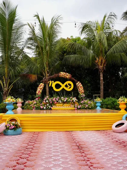 A modern and playful Mehendi stage. The infinity symbol with the couple's initials, set against a bright yellow stage, symbolizes their forever love story in a fun and contemporary way.