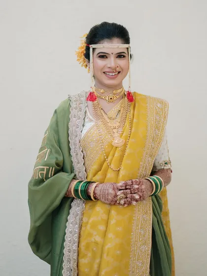 A full-length portrait of a Marathi bride in a beautiful yellow saree. Her hands joined in a traditional greeting, she exudes grace and warmth.
