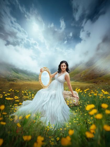 Adding a vintage mirror as a prop creates a touch of whimsy and reflection. This artistic shot in a field of yellow flowers is part of a conceptual maternity series.