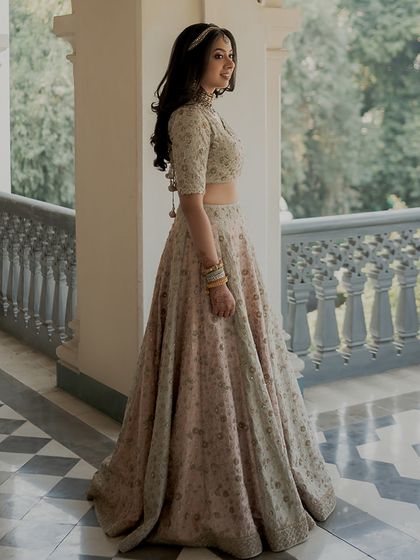 A full-length portrait of a bride in a dreamy, vintage-toned pastel lehenga. The soft, radiant glam enhances her natural beauty and is designed to last through every moment.
