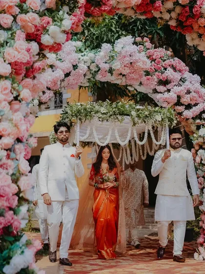 A breathtaking entry through a floral archway. The bride looks like a princess in her beautiful saree and long veil.