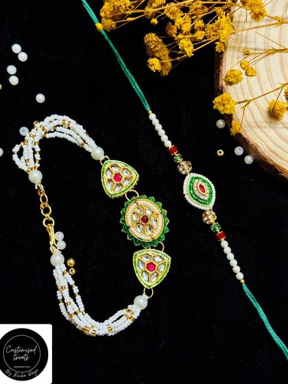 An elegant kundan rakhi set with green and red stones. The Lumba features three beautiful motifs on a pearl strand, paired with a matching single-motif rakhi.