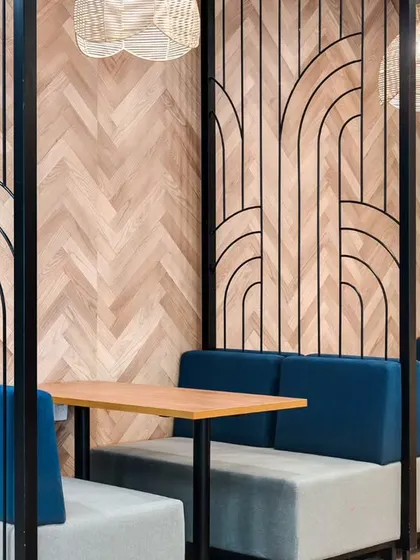 Semi-private meeting pods with comfortable booth seating. The decorative metal screens and herringbone wood-patterned walls create a sophisticated and visually interesting design.