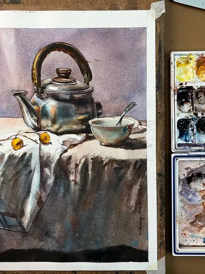 A still life of a metal teapot and a cup, focusing on capturing the metallic reflections and the soft folds of the fabric.