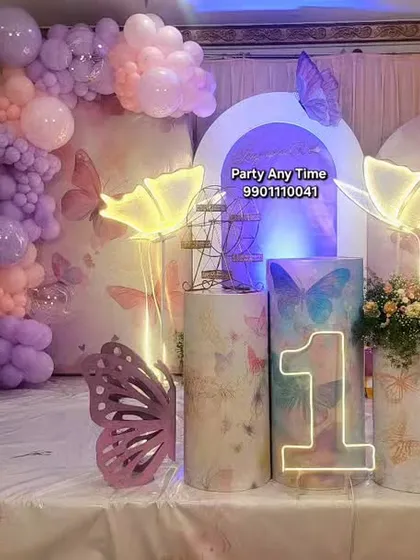 The full setup for the butterfly theme, including a milestone board showing the baby's first year, themed backdrops, and a light-up number '1'.