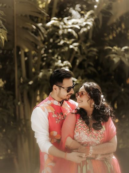 A cozy and intimate embrace. The couple holds each other close, sharing a quiet moment away from the crowd, framed by the lush greenery of the venue.