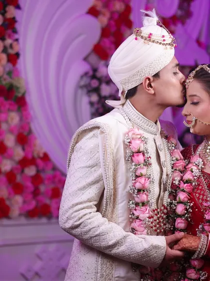 A sweet kiss on the forehead, set against a beautifully decorated floral backdrop. A perfect romantic wedding portrait.
