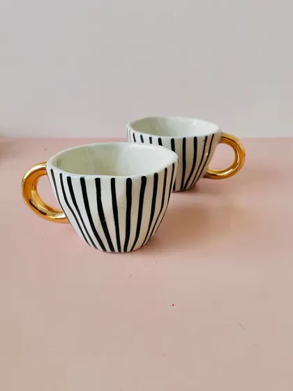 A close-up of the premium ceramic cups with black and white stripes and a gold handle. They are a stylish addition to any hamper.