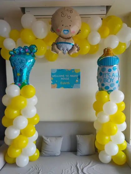A sweet 'Welcome to Nani House' setup for a baby boy. It includes yellow and white balloon pillars, baby-themed foil balloons, and a personalized welcome sign.