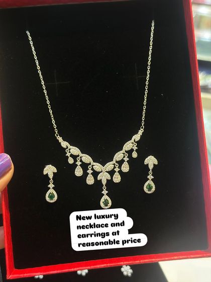 This silver necklace set features delicate leaf-like patterns with dangling green stones. It's a perfect accessory for festive occasions.