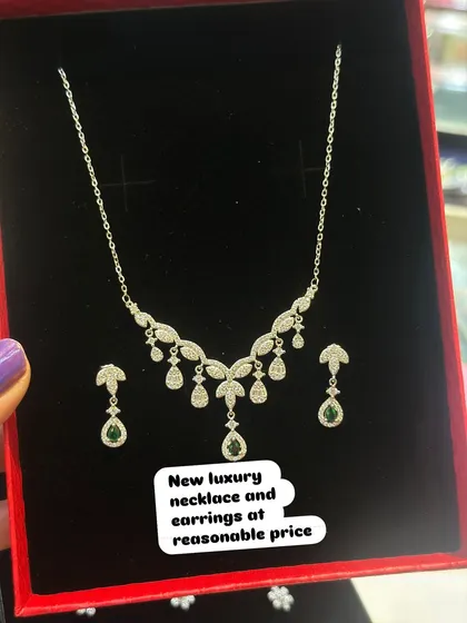 This silver necklace set features delicate leaf-like patterns with dangling green stones. It's a perfect accessory for festive occasions.