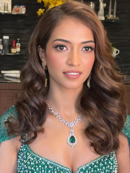A glamorous look for a Sangeet or reception. The client's hair is styled in classic Hollywood waves, giving her a sophisticated and polished appearance that pairs perfectly with her emerald green gown.