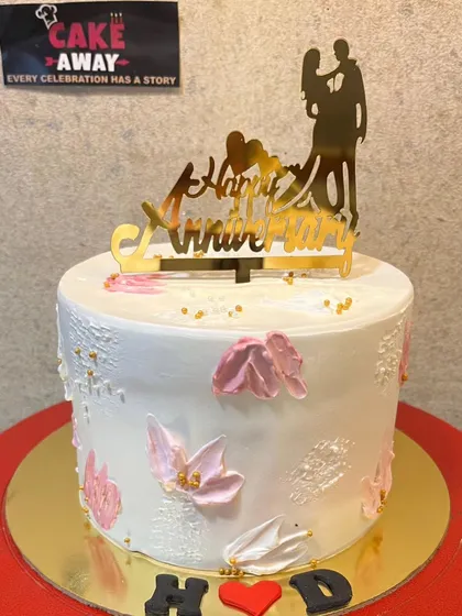 An elegant white anniversary cake with delicate pink floral details and a silhouette-style couple topper.