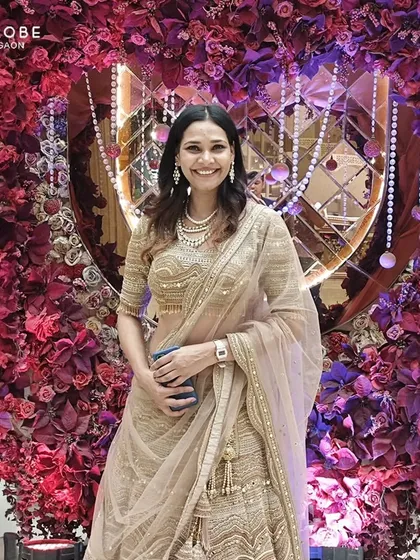 This client is glowing in a beige and gold lehenga, standing against a beautiful floral backdrop. It's a classic and elegant choice for a reception.
