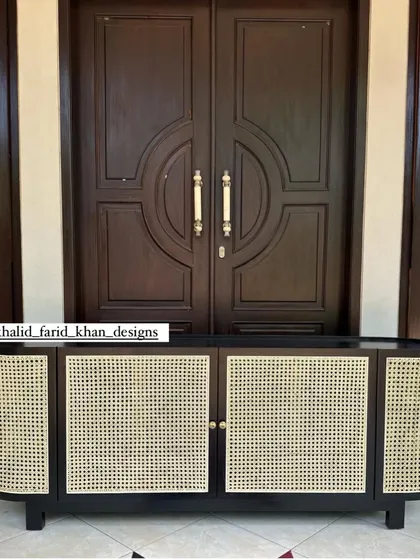 The oval-shaped black and cane sideboard, shown in front of an ornate door.