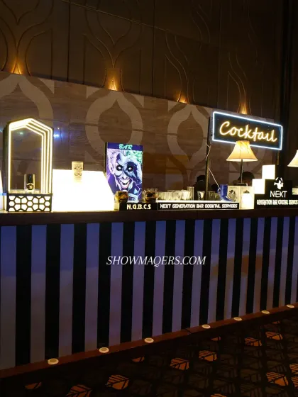 A close-up of the stylish cocktail bar at the masquerade-themed event. The black-and-white stripes, neon sign, and table lamps create a chic, retro vibe.