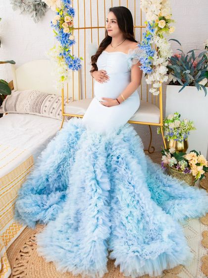 A vision of tranquility. This mother-to-be is seated in a dreamy setup, her light blue ruffled gown spreading out like a cloud. The floral decor and soft lighting enhance the magical quality of the portrait.