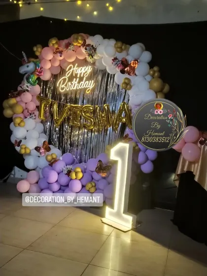 A magical unicorn theme for a first birthday party. This setup features a circular backdrop with a silver fringe, a custom neon "Happy Birthday" sign, foil letters for the name, and a large light-up number '1' to mark the special milestone.