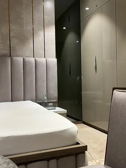 This view of the Juhu bedroom highlights the sleek, high-gloss wardrobes and the soft, upholstered headboard. The design focuses on a calm, neutral palette enriched with varied textures for a luxurious feel.