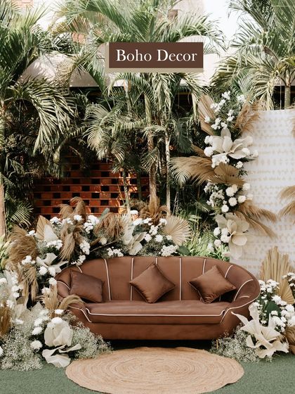 A beautiful boho-chic seating area for a Haldi ceremony, featuring a comfortable brown sofa surrounded by pampas grass and white floral arrangements.