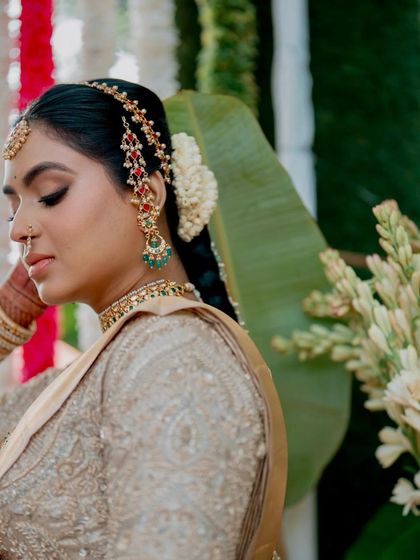 A close-up of a bride's profile, highlighting her traditional hairstyle and jewelry. Her golden silk saree and matching embroidered blouse were custom-designed to create a look of timeless elegance.