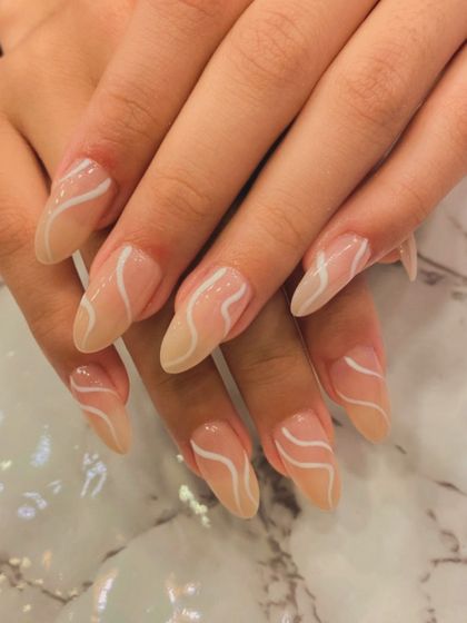 A minimalist and elegant design on long, stiletto nails. The sheer nude base is decorated with fine, wavy white lines for a simple yet artistic look.