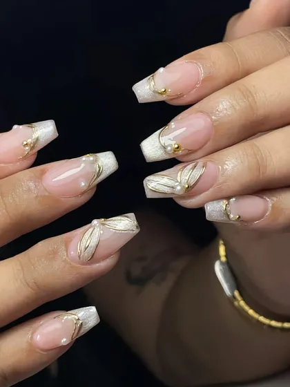 Square-tipped French manicure with 3D gold leaf accents and pearls. This is a modern and luxurious take on a classic style.