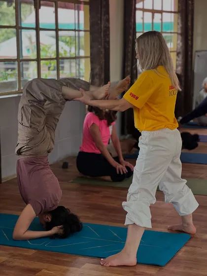 A teacher assists a student in the scorpion pose, helping her find balance and proper alignment. This level of personal attention is key to our teaching methodology.