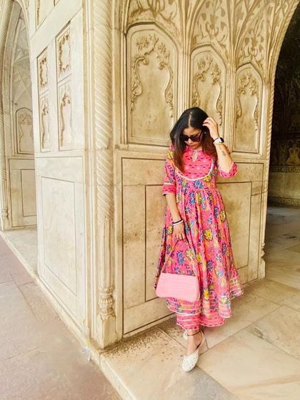 A candid moment captured within the beautiful archways of the Taj Mahal complex. The vibrant pink floral anarkali suit feels right at home against the intricate marble work, blending color with history.
