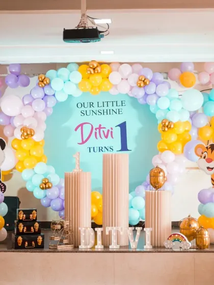 A closer view of the "Our Little Sunshine" first birthday decor. The pastel balloon arch in shades of blue, purple, and yellow is accented with gold foil balloons for a touch of sparkle.