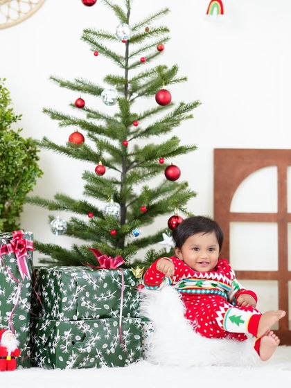 A festive Christmas-themed shoot with a baby boy in a cute holiday sweater, sitting by a Christmas tree and presents.